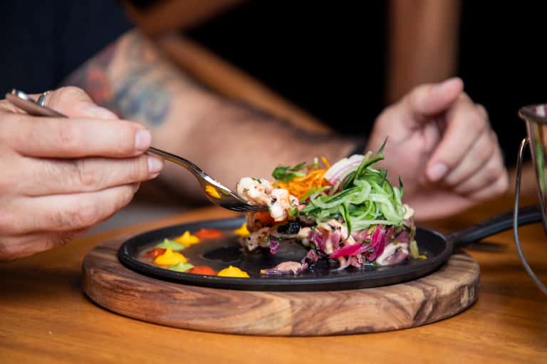 Close-up of plated seafood dish with purple cabbage and microgreens on dark plate