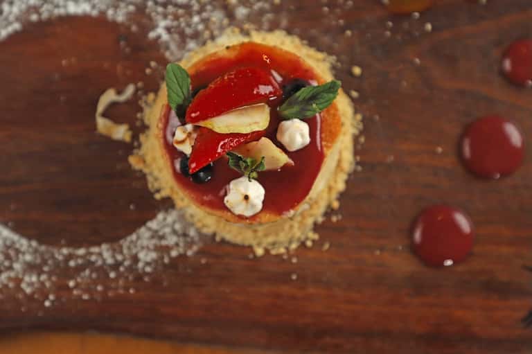 Gourmet dessert tart with red glaze, apple slices, and mint on wooden surface