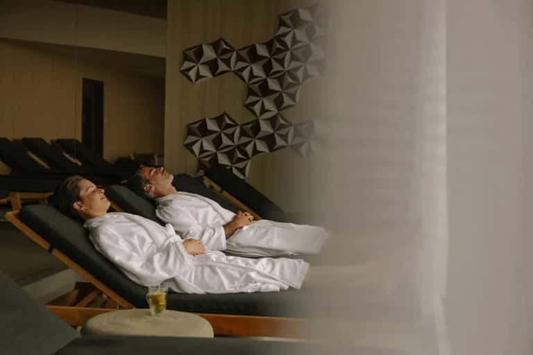 Two guests relaxing on black lounge chairs in spa relaxation room with geometric wall art