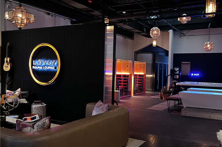 Modern entertainment venue with neon sauna lounge sign, hanging light fixtures, and bowling lanes.