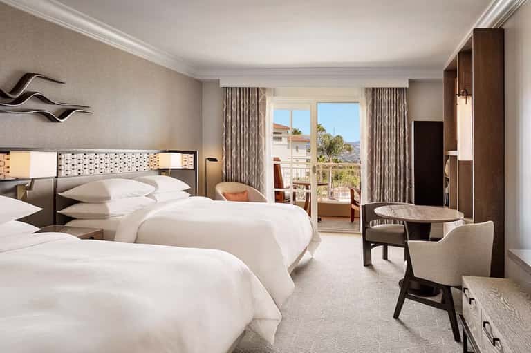 Upscale hotel room with two queen beds, balcony view, and contemporary furnishings