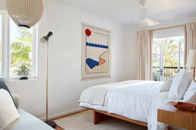Minimalist hotel bedroom with white bedding, woven pendant light, and balcony view