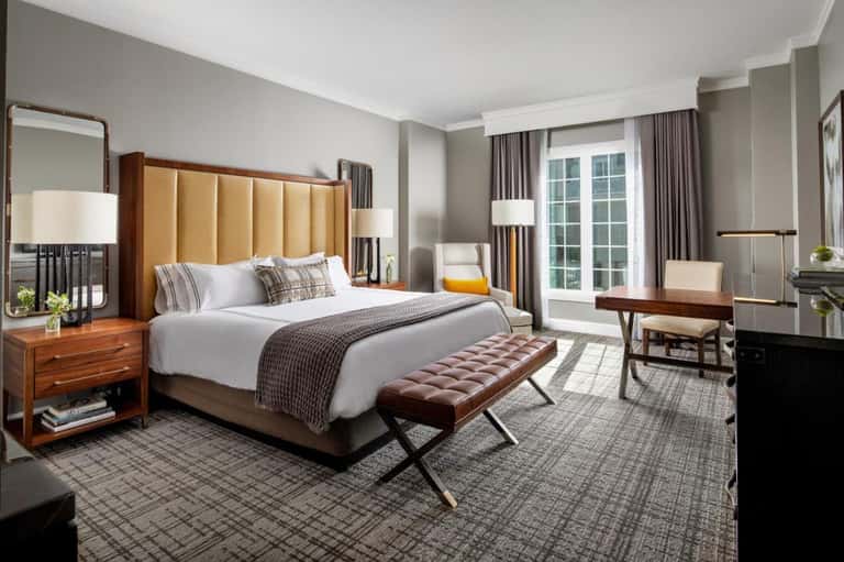Luxurious hotel bedroom with gold headboard, wood nightstands, elegant furnishings, and balcony access