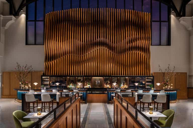 Modern hotel bar with sculptural wood feature wall, pendant lighting, and elegant seating