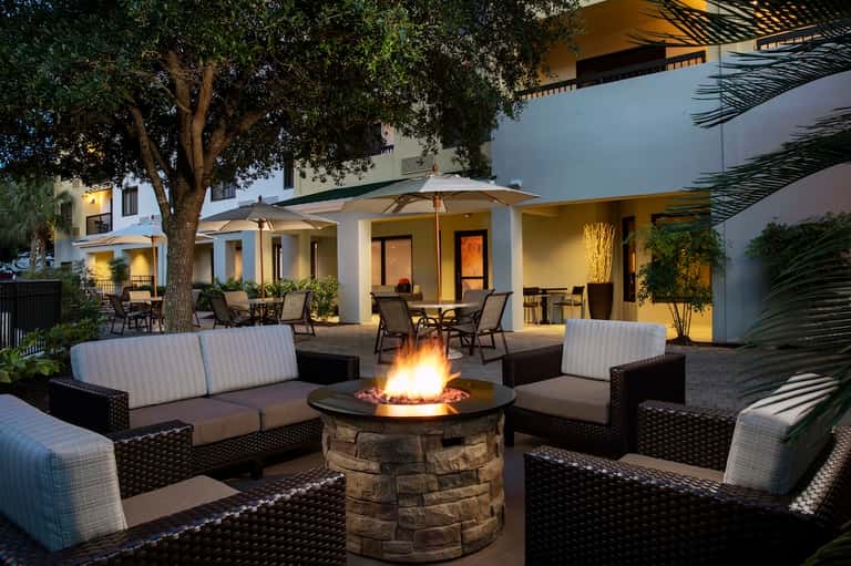 Outdoor patio area with fire pit, lounge seating, palm trees, and illuminated modern architecture