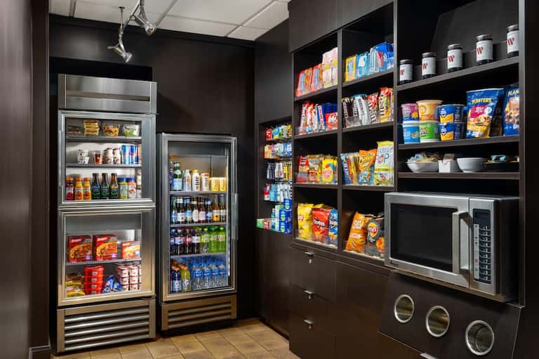 Hotel snack bar with glass-front refrigerators, shelving with beverages and snacks, and microwave