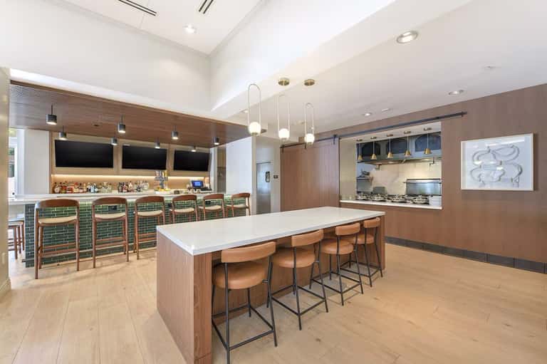 Modern kitchen and bar with wood cabinetry, green tile, and pendant lighting