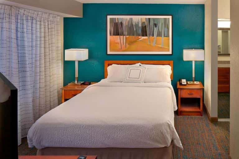 Hotel bedroom with teal accent wall, orange wood nightstands, and white bedding