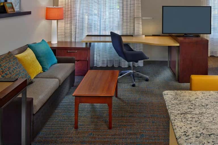 Modern hotel suite with sofa, desk, TV, and colorful accent pillows in warm tones