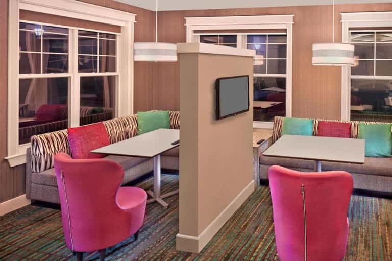 Colorful hotel lounge with pink chairs, multi-colored pillows, and windows overlooking water
