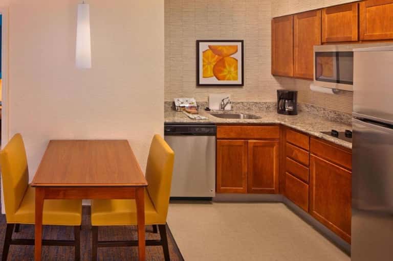 Hotel suite kitchenette with wood cabinets, granite counters, and yellow dining chairs