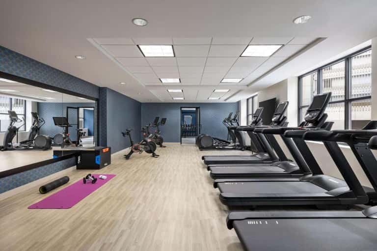 Spacious fitness center with treadmills, exercise bikes, blue accent walls, and large windows