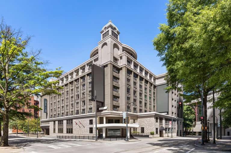 Historic stone hotel building with distinctive tower architecture on tree-lined street