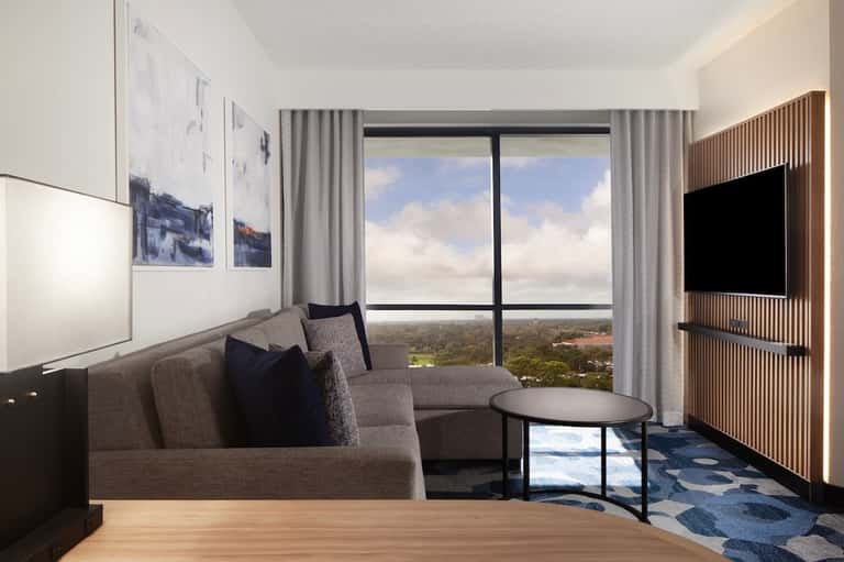 Luxury hotel suite living room with gray sofa, floor-to-ceiling windows overlooking landscape