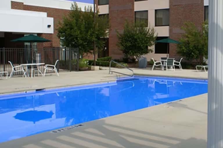 Rectangular pool with lounge chairs and umbrellas on brick patio surrounded by modern brick building