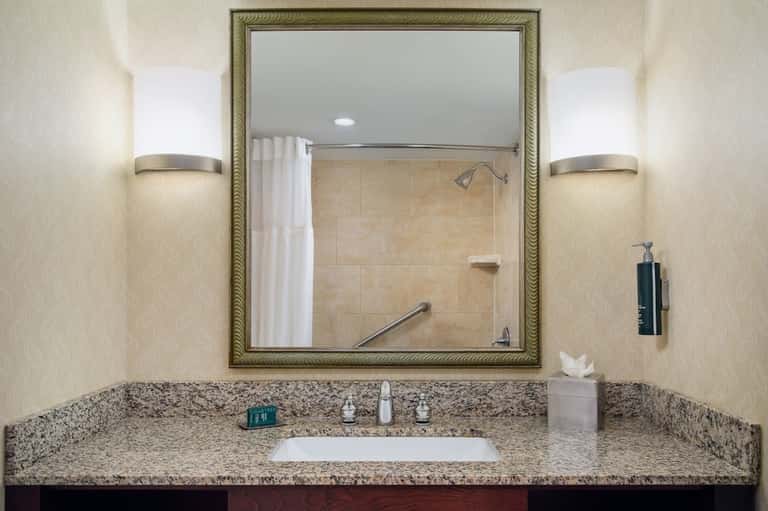 Hotel bathroom vanity with granite countertop, framed mirror, and wall sconces
