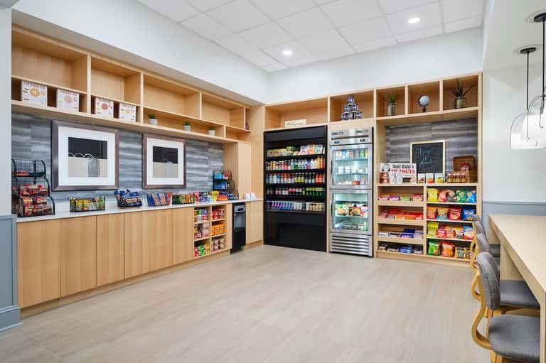 Modern hotel market shop with wooden shelving, refrigerated beverages, and snack displays