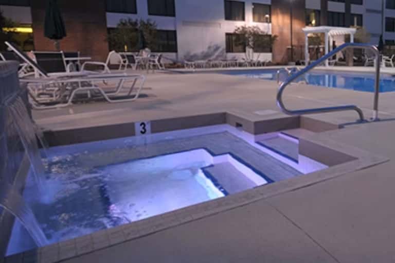 Illuminated hot tub at night with stairs and lounge chairs on pool deck