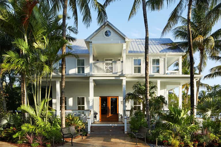 Elegant white two-story home with columns, metal roof, and palm tree landscaping