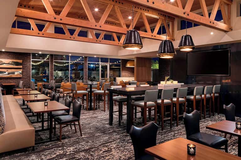 Modern indoor lounge with exposed wood beams, pendant lights, and floor-to-ceiling windows