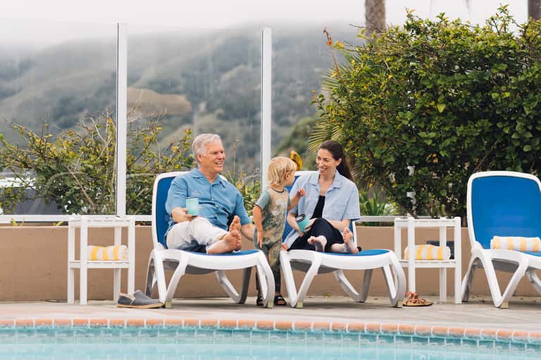 Family relaxing on blue lounge chairs by outdoor pool with mountain valley views