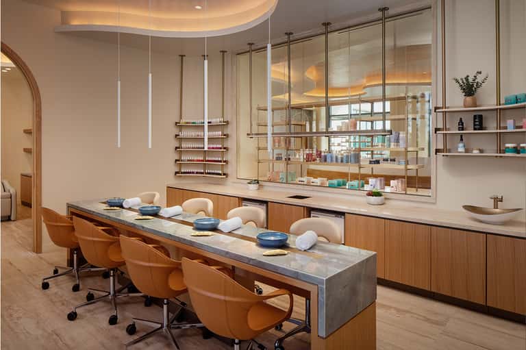 Modern salon interior with wooden counter, orange chairs, pendant lighting, and product display shelving