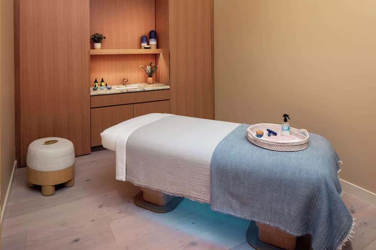 Spa treatment room with massage table, wooden accents, and amenity shelves