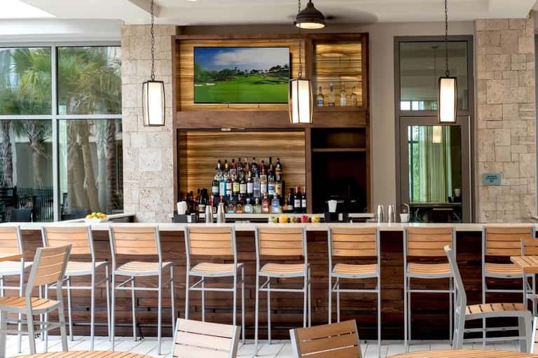 Modern resort bar with wood paneling, spirits display, and golf course view