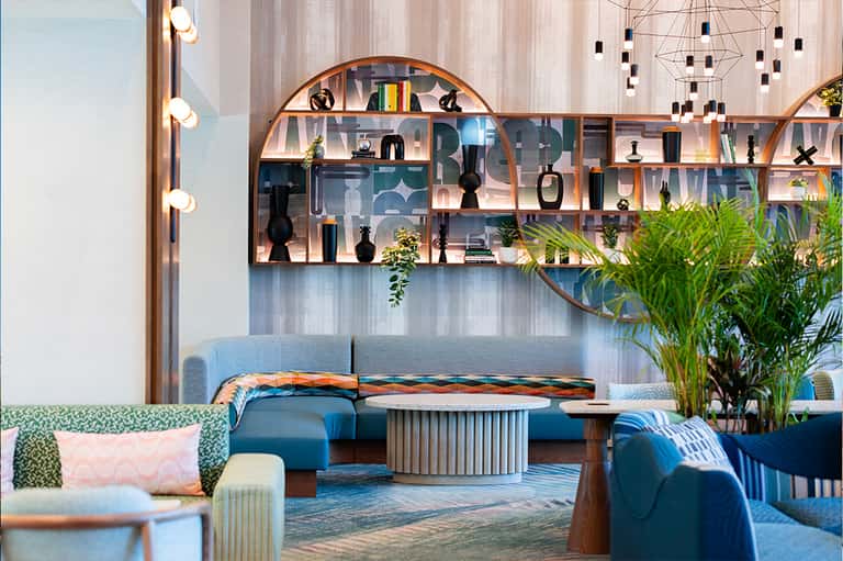Modern hotel lobby with curved shelving, blue seating, decorative objects, and hanging lights