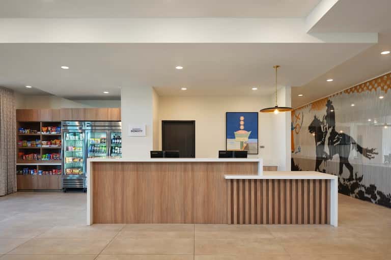 Modern hotel reception desk with wood paneling, beverage coolers, and contemporary lounge seating