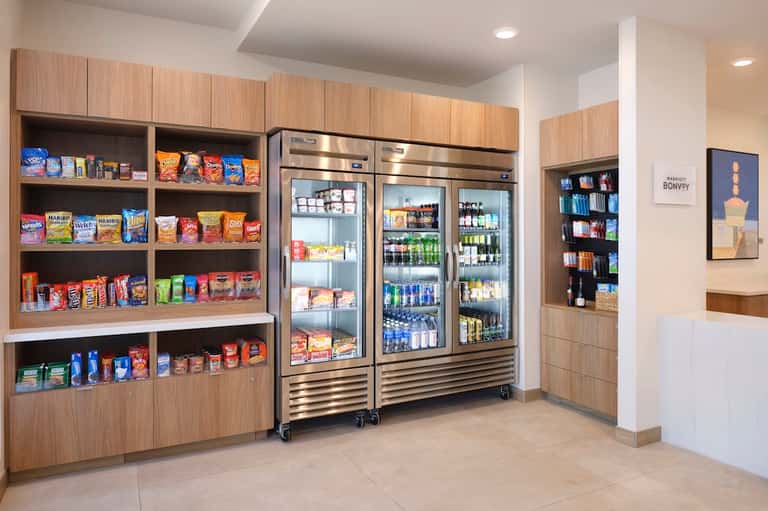 Hotel convenience store with wooden shelving, snacks, beverages, refrigerated cases, and drink coolers