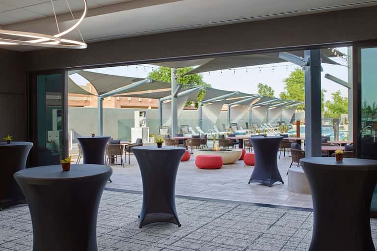 Modern outdoor event space with black tables, shade sails, and lounge seating on a patio