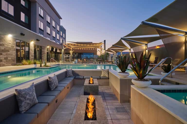 Luxury resort pool at dusk with fire pits, lounge seating, and illuminated hotel building
