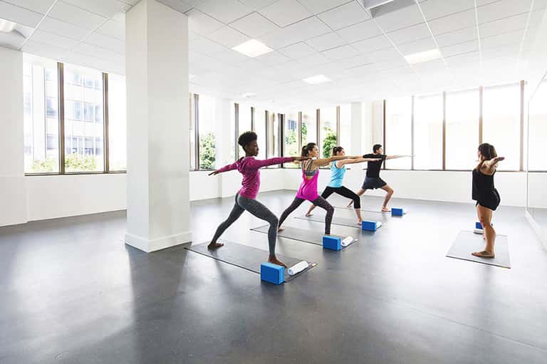 Fitness studio with five women performing yoga poses on mats with blue blocks during group class