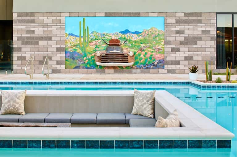 Resort pool deck with colorful desert mural, lounge area, and mountain view seating