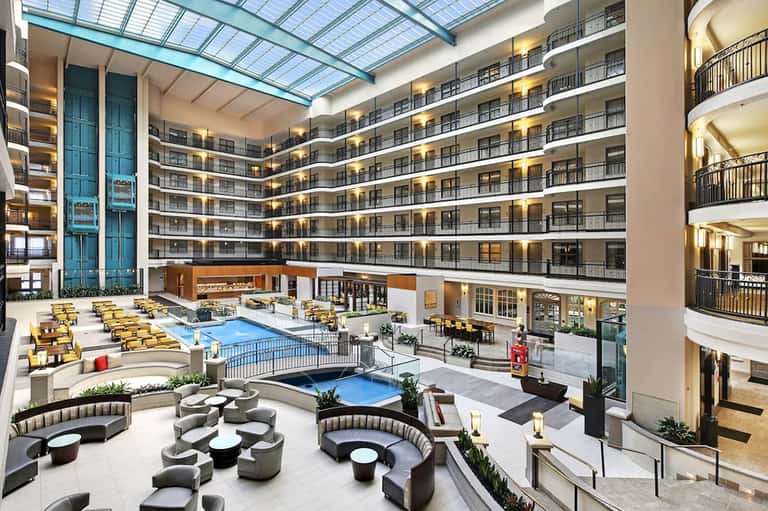 Hotel indoor pool complex with surrounding guest rooms, lounge seating, and glass ceiling