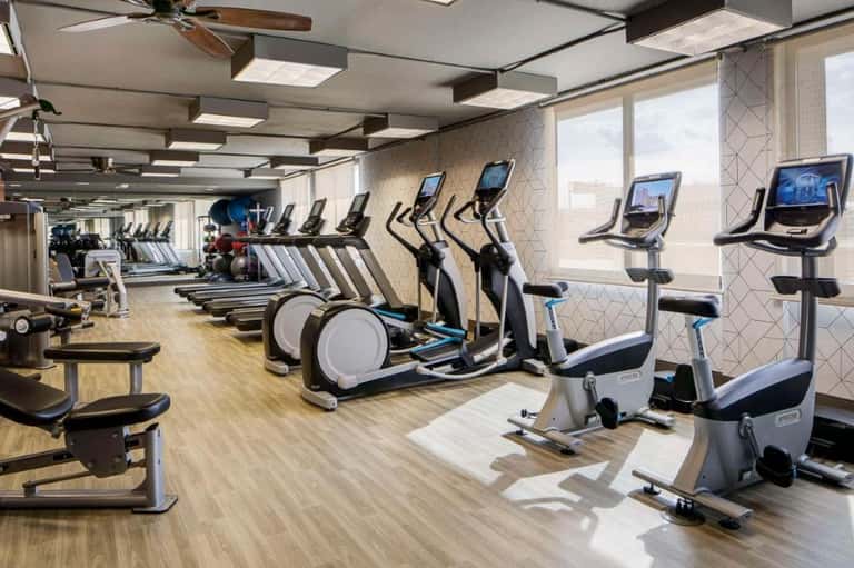Contemporary fitness center with rows of stationary bikes, elliptical machines, and large windows
