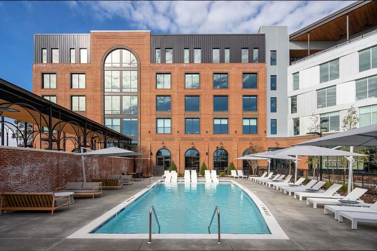 Resort pool courtyard with brick building, white lounge chairs, and umbrellas in contemporary setting