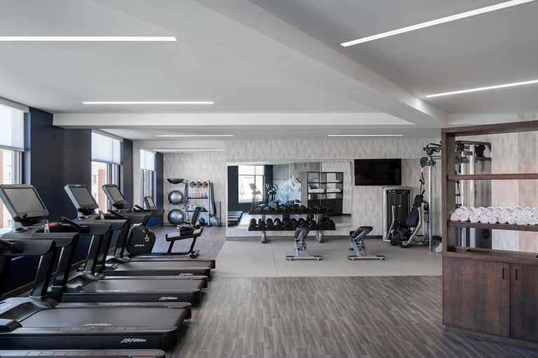 Modern fitness center with treadmills, cardio equipment, weights, and TV screens
