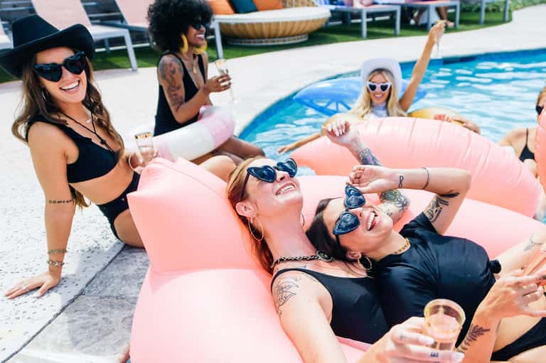 Pool party with guests on pink floats, colorful swimwear, and festive atmosphere