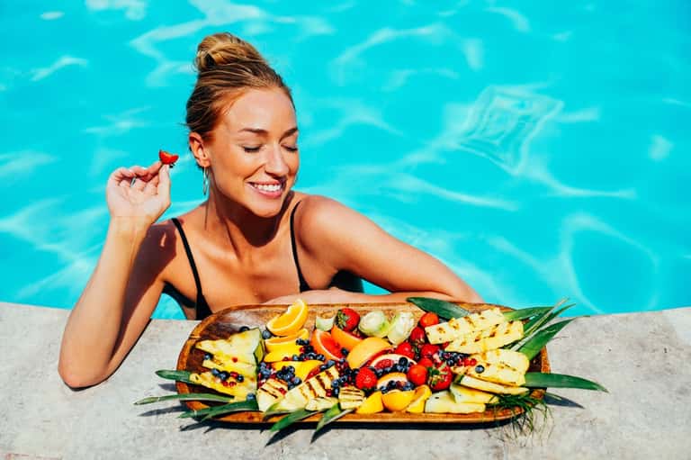 Woman at pool edge enjoying grilled fruit platter with colorful vegetables