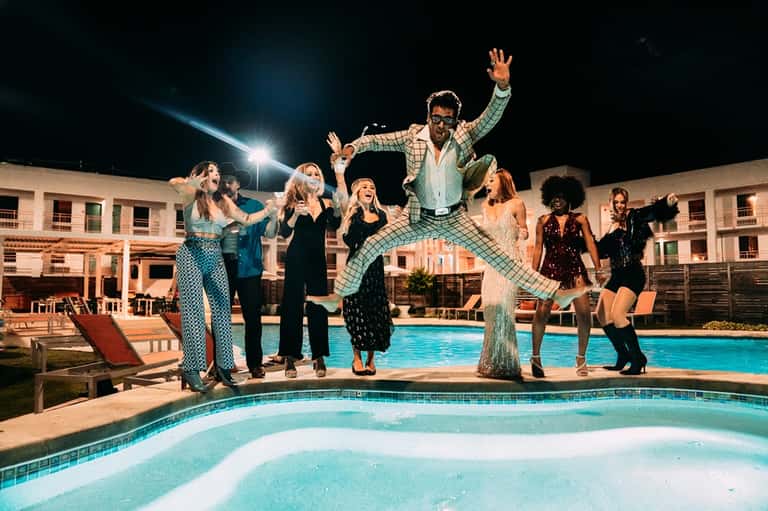 Group of guests celebrating at poolside during evening event at resort with lit buildings