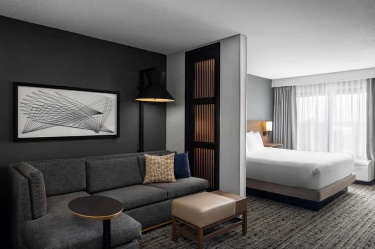 Contemporary hotel suite with dark accent wall, gray sofa, king bed, and minimalist furnishings