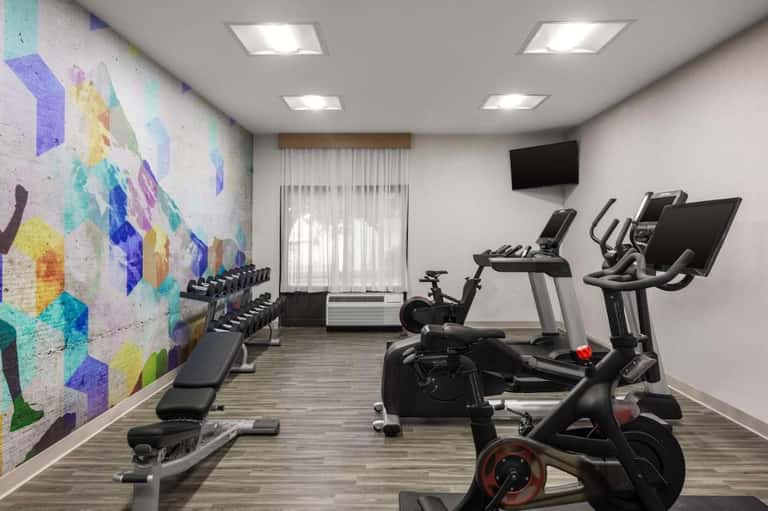 Hotel fitness center with cardio equipment, colorful abstract wall mural, and exercise bikes