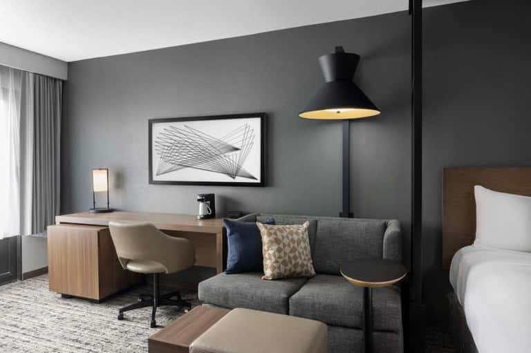 Hotel room with modern gray walls, wooden desk, gray sofa, and pendant lighting