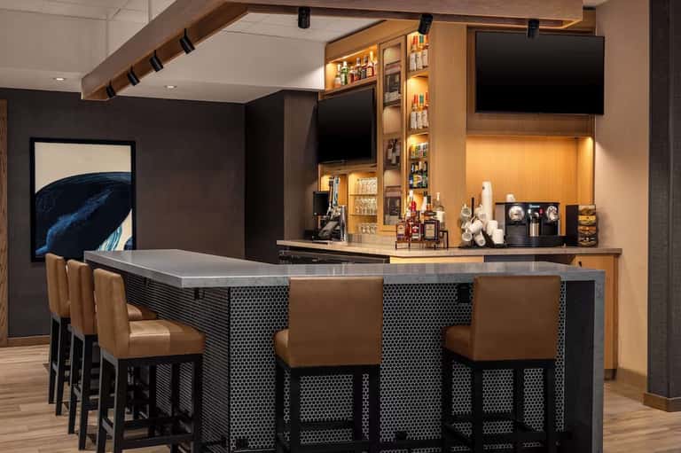 Contemporary home bar with dark cabinetry, brass accents, leather bar stools, and stocked shelving