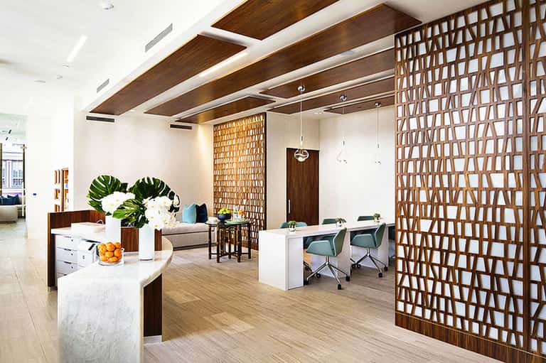 Modern office reception area with wooden ceiling beams, white desks, geometric wooden screens, and contemporary furnishings