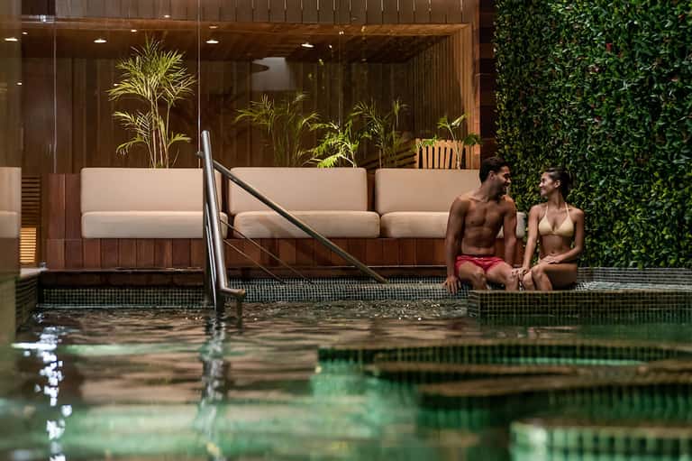 Modern spa pool with wooden lounge chairs, ivy wall, and minimalist design