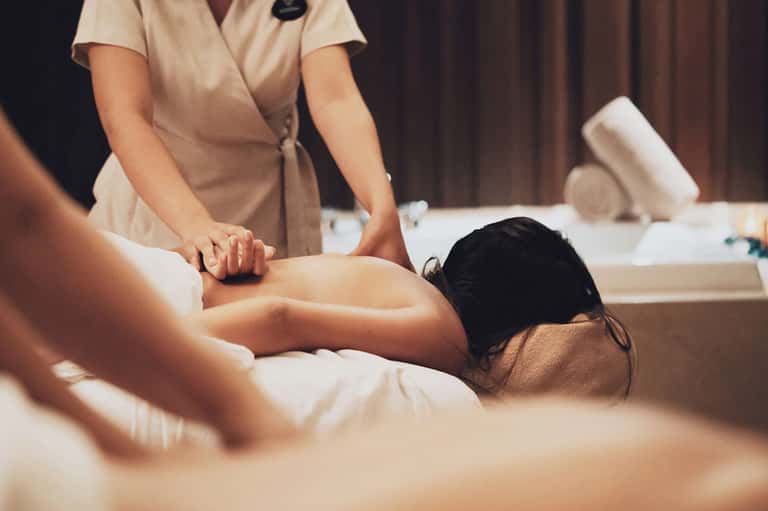 Spa therapist giving massage treatment to client on white massage table in serene indoor wellness room