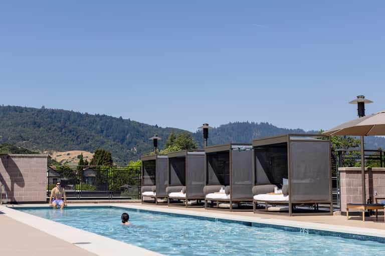 Resort pool with mountainous backdrop, modern cabanas with seating, and guests enjoying the water